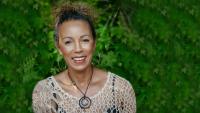 Founder and CEO of SMB Essentials, Lake Louise, smiles at the camera. She is wearing a crocheted beige top, large hoop earrings, and a handmade circle necklace. 